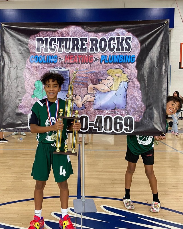 A boy holding the trophy in front of a Picture Rocks banner.